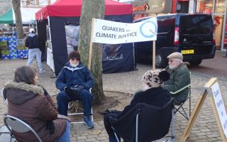 Quakers at our Vigil for Climate Justice seated in a circle under the banner in the Aylesbury Market Square.