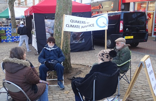 Quakers at our Vigil for Climate Justice seated in a circle under the banner in the Aylesbury Market Square.